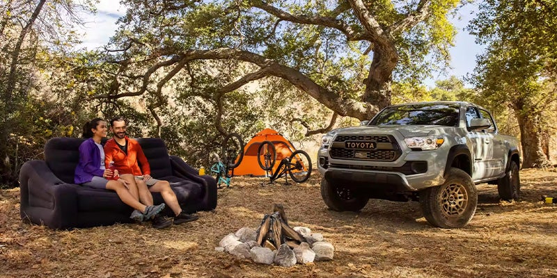 2 people sitting near a 2023 Toyota Tacoma at a campsite.