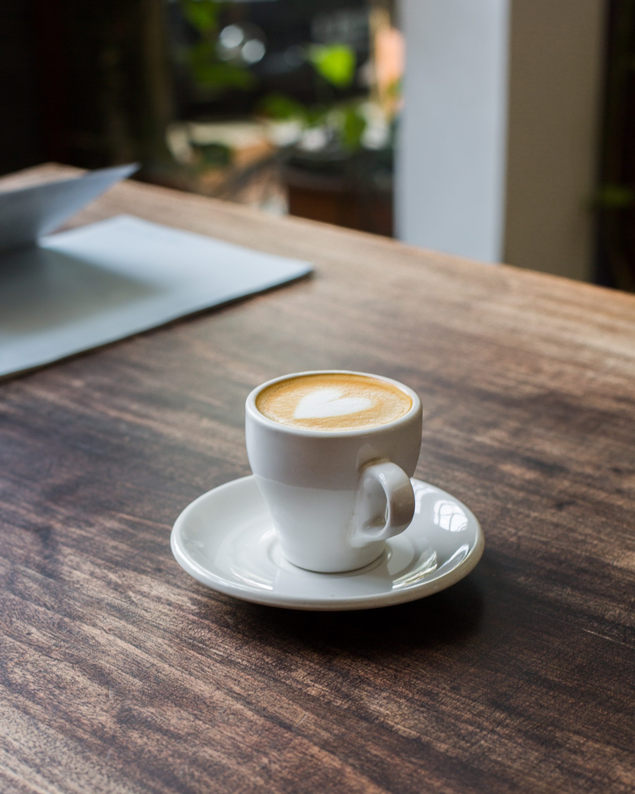A latte in a white cup sitting on a wooden table.